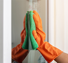 Person cleaning glass window with glove and microfiber cloth